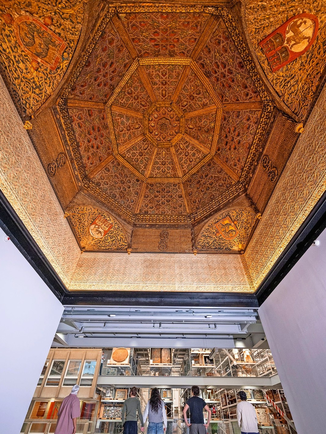 Photo of a 15th-century gilded wooden ceiling from the now-lost Torrijos Palace in Spain, viewed from below by several people looking into a museum storage area.