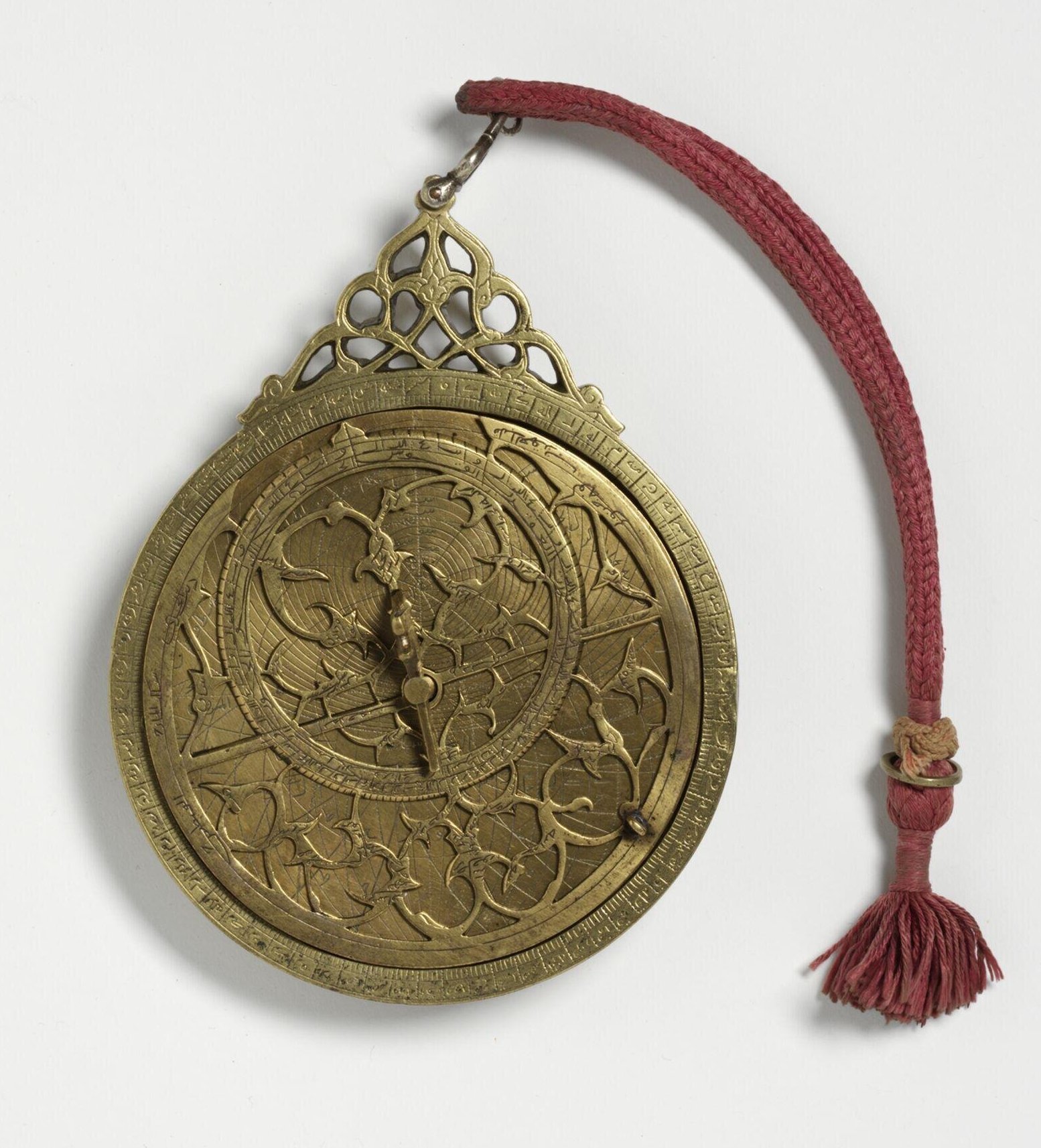 Circular brass astrolabe with six internal plates and a red suspension cord, made in Iran.