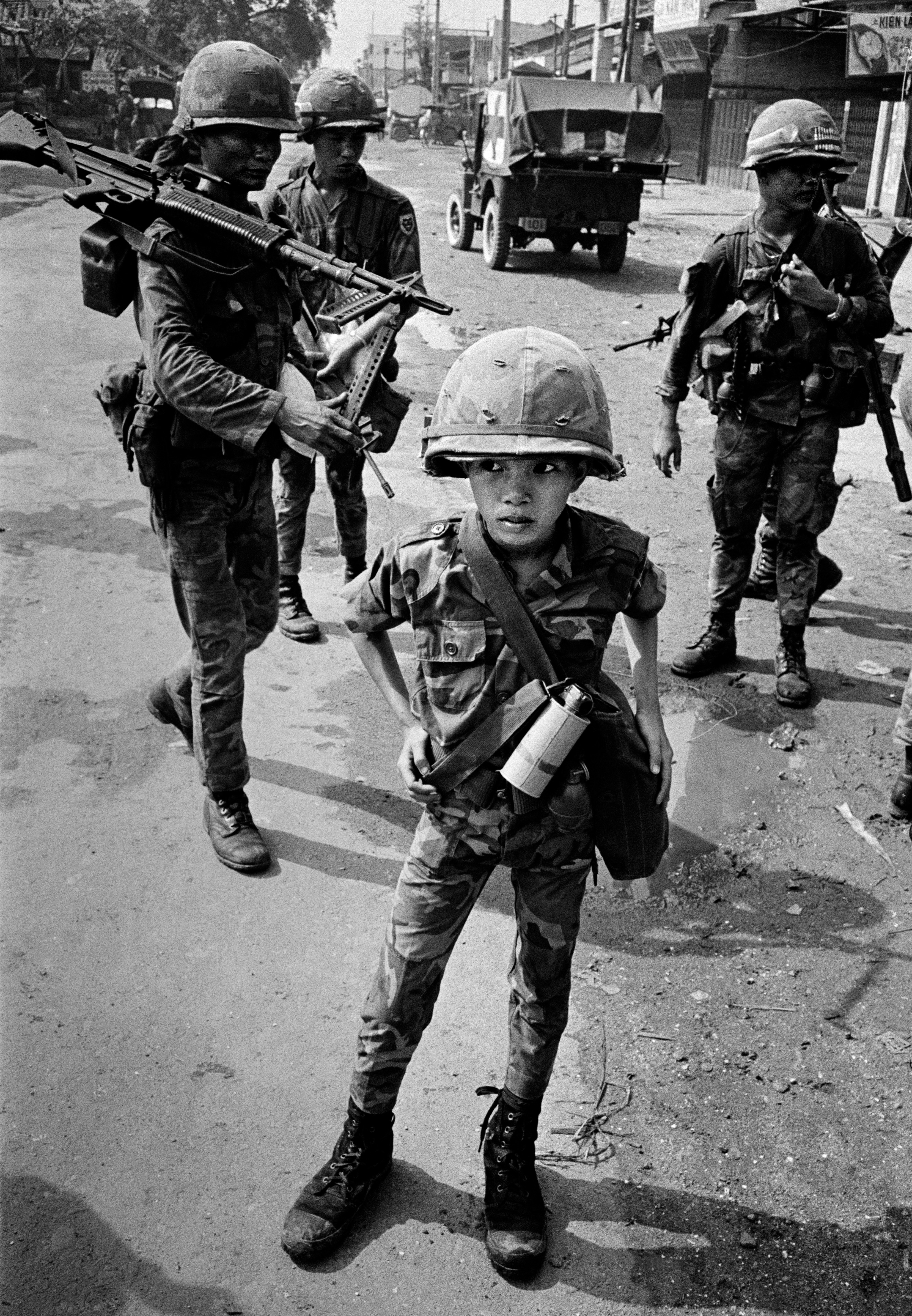 A young boy in military attire in the streets of Vietnam.