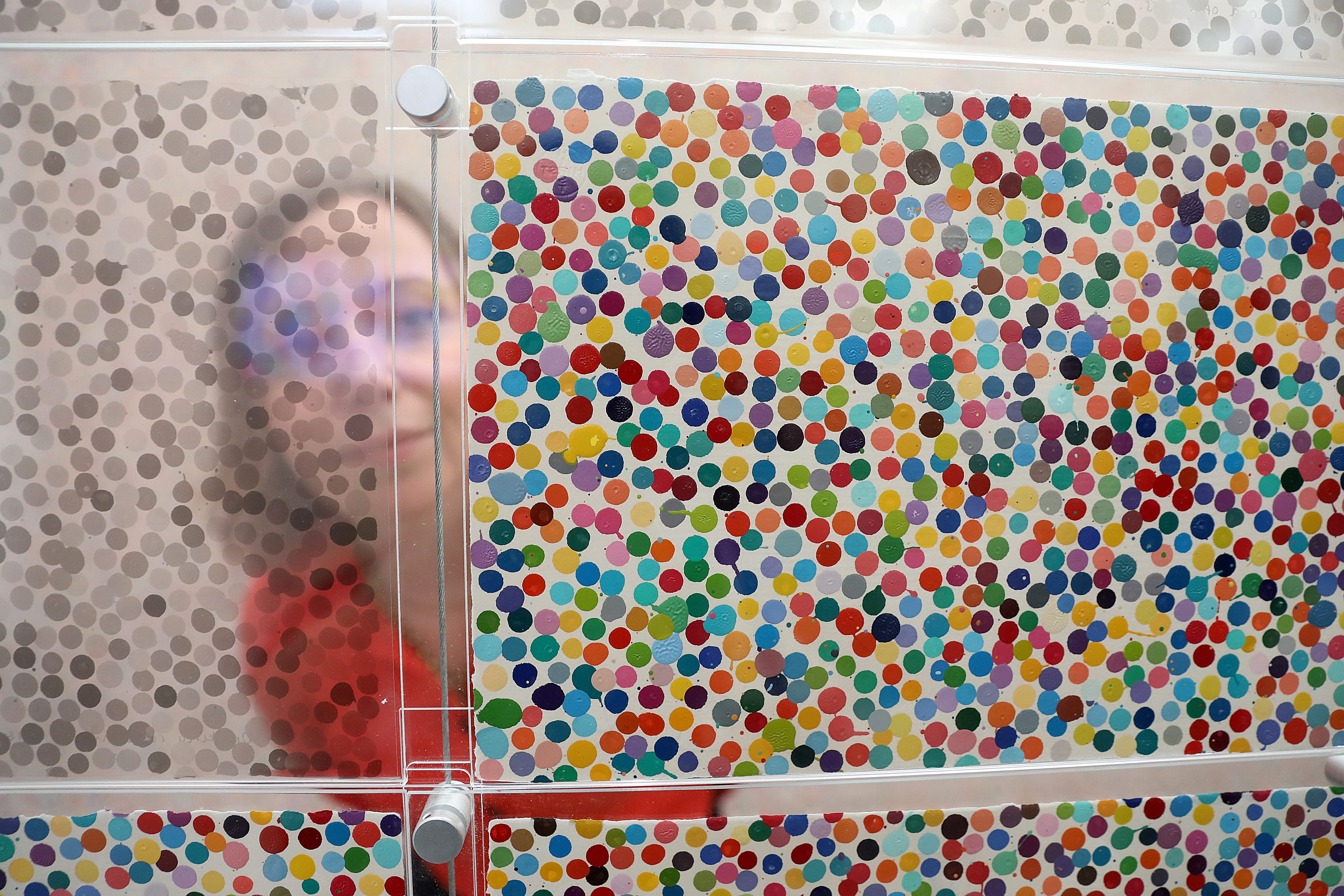 A gallery assistant partially obscured behind a display of Damien Hirst's 