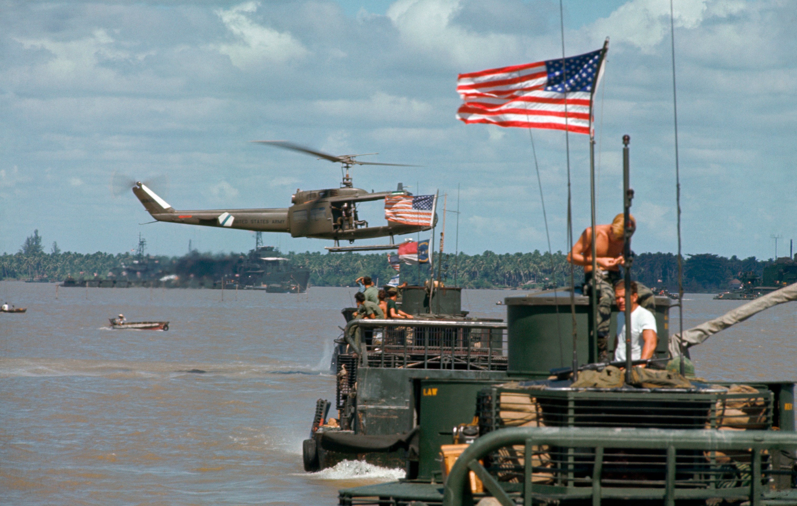 A US Navy gunboat in Vietnam with a helicopter in the air overhead.