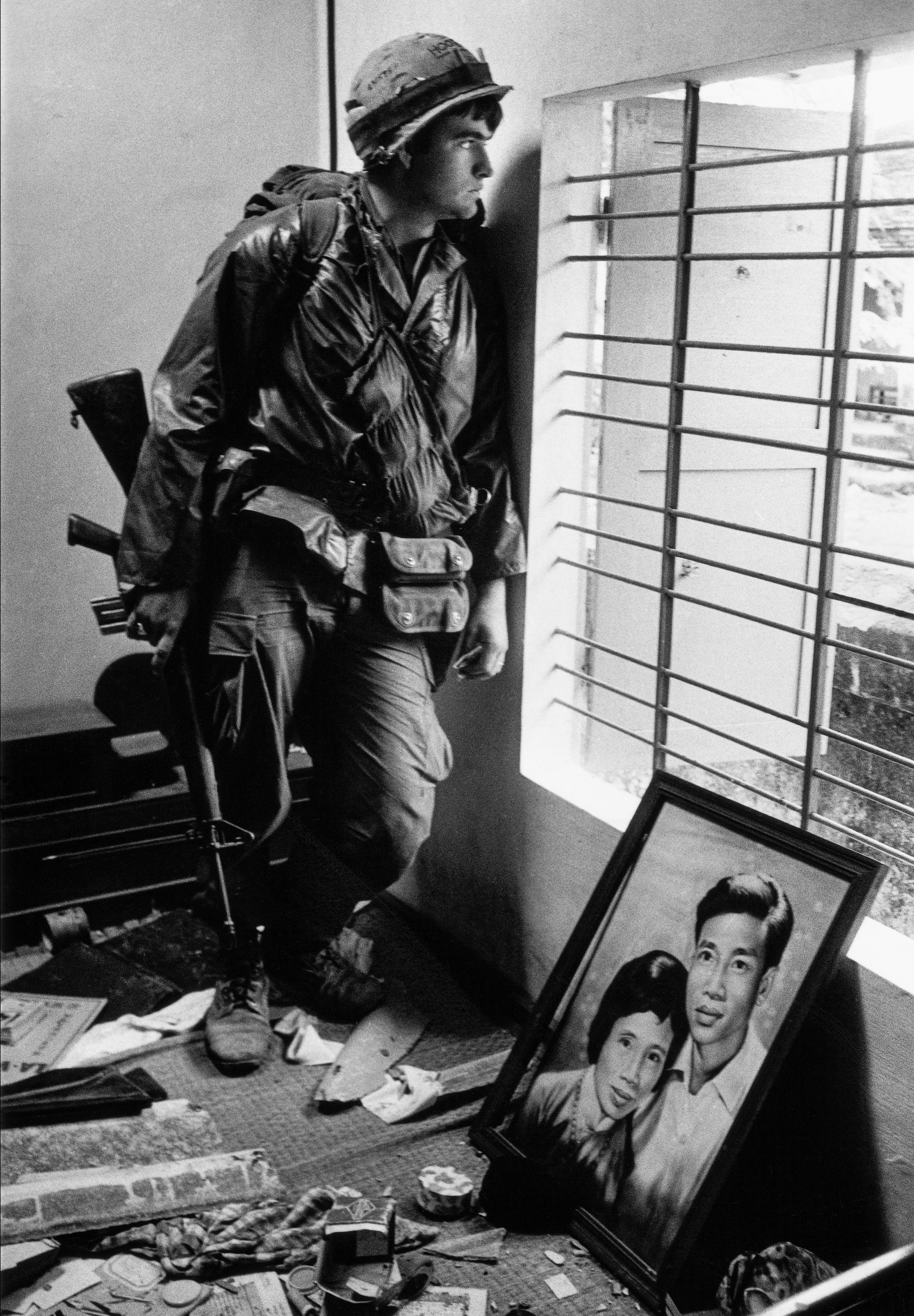 A soldier rests against a wall during the Tet Offensive in Hue, Vietnam; a portrait of a couple lies on the floor.