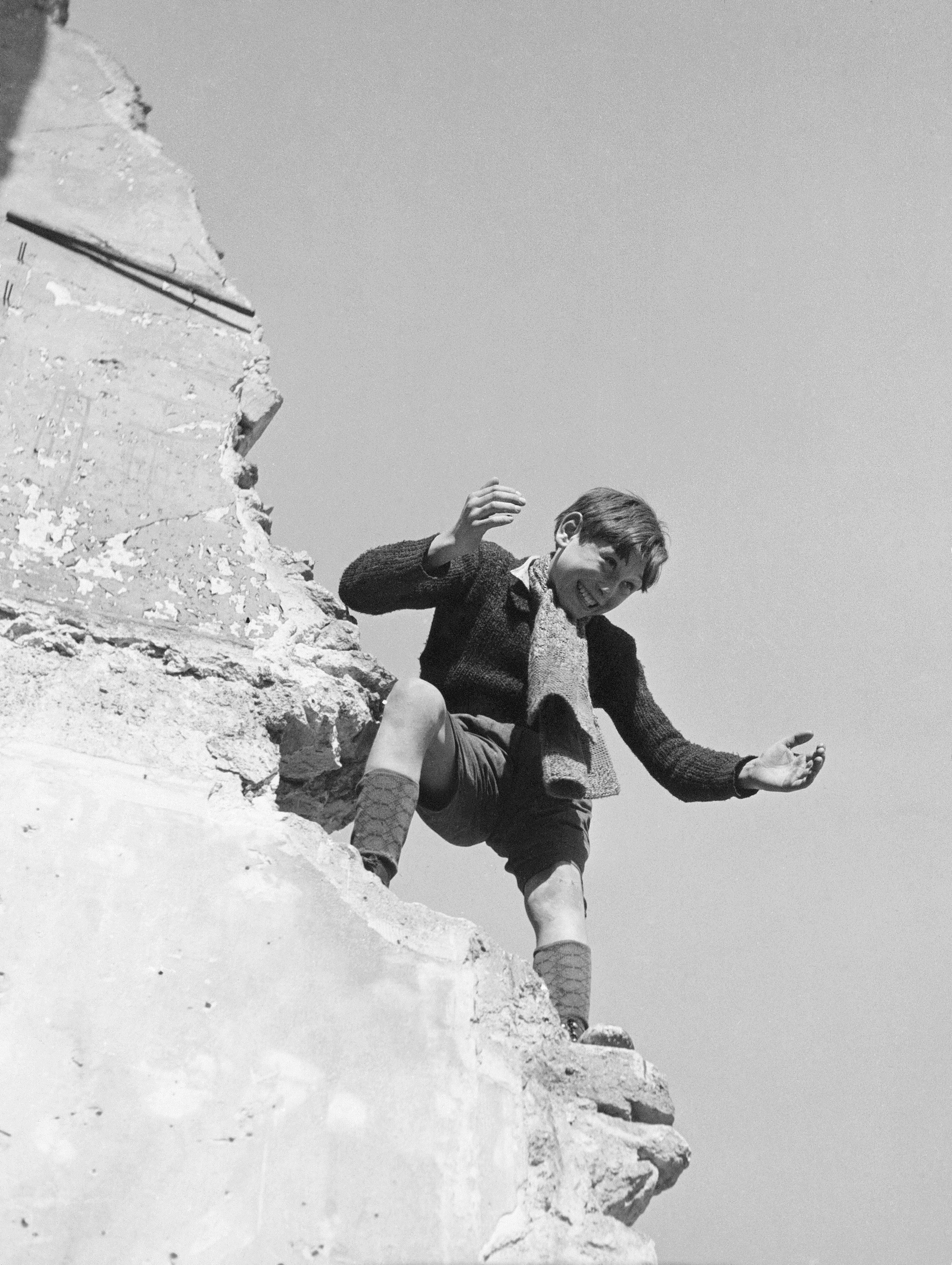 Black and white photo of a boy perched on a crumbling wall.
